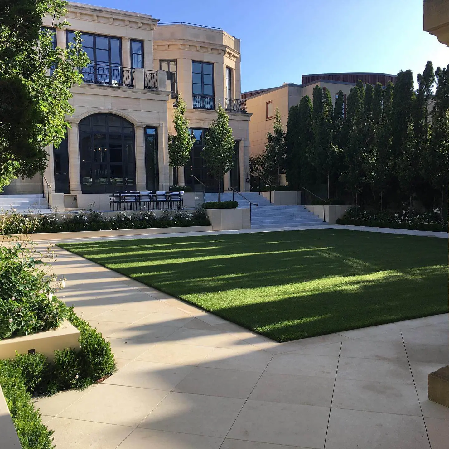 Luxury estate backyard with manicured artificial turf, stone terrace, and formal landscaping