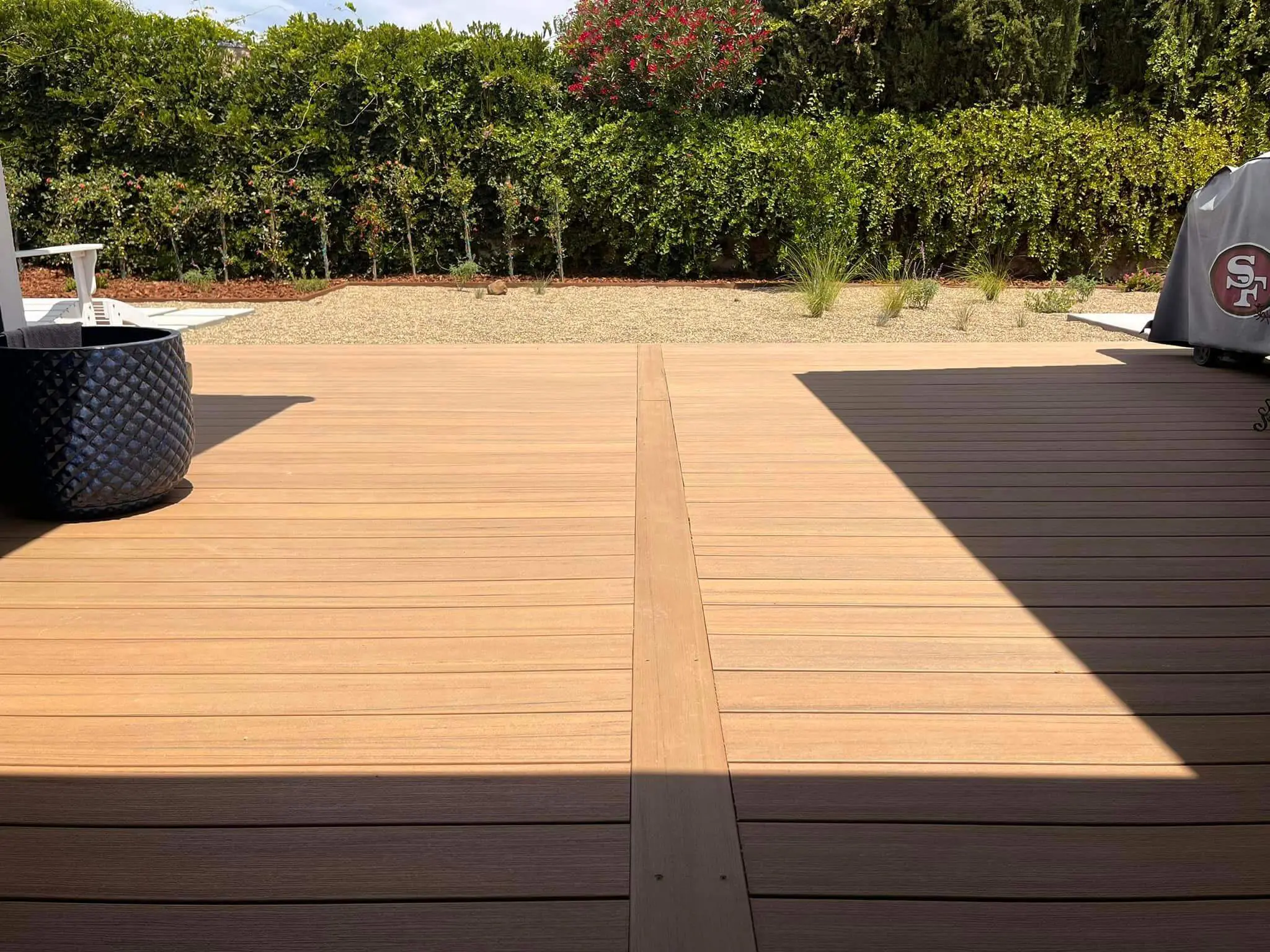 Two-tone composite wood deck with gravel garden bed and green hedges in the background