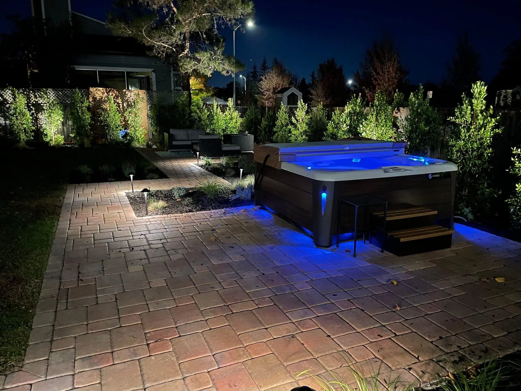 Illuminated backyard hot tub with blue LED lighting on a brick paver patio at night