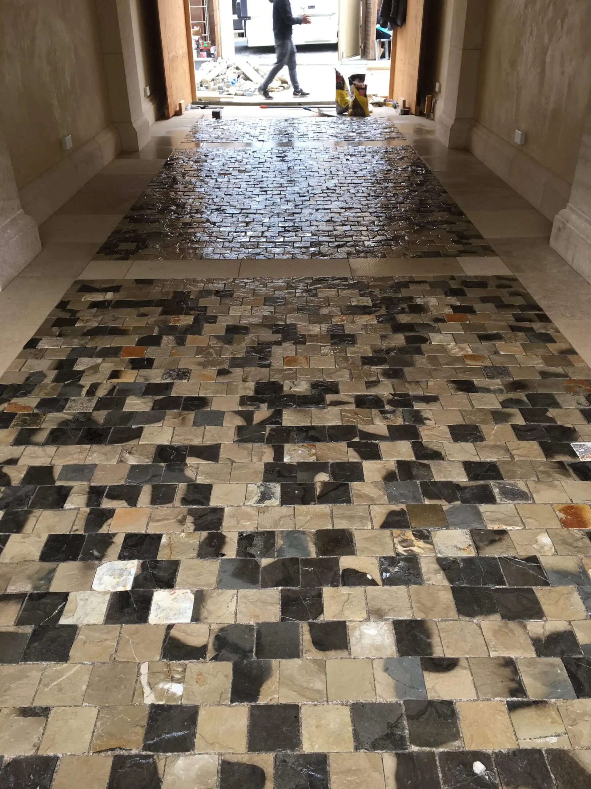 Decorative mosaic stone tile flooring being installed in an entryway hallway