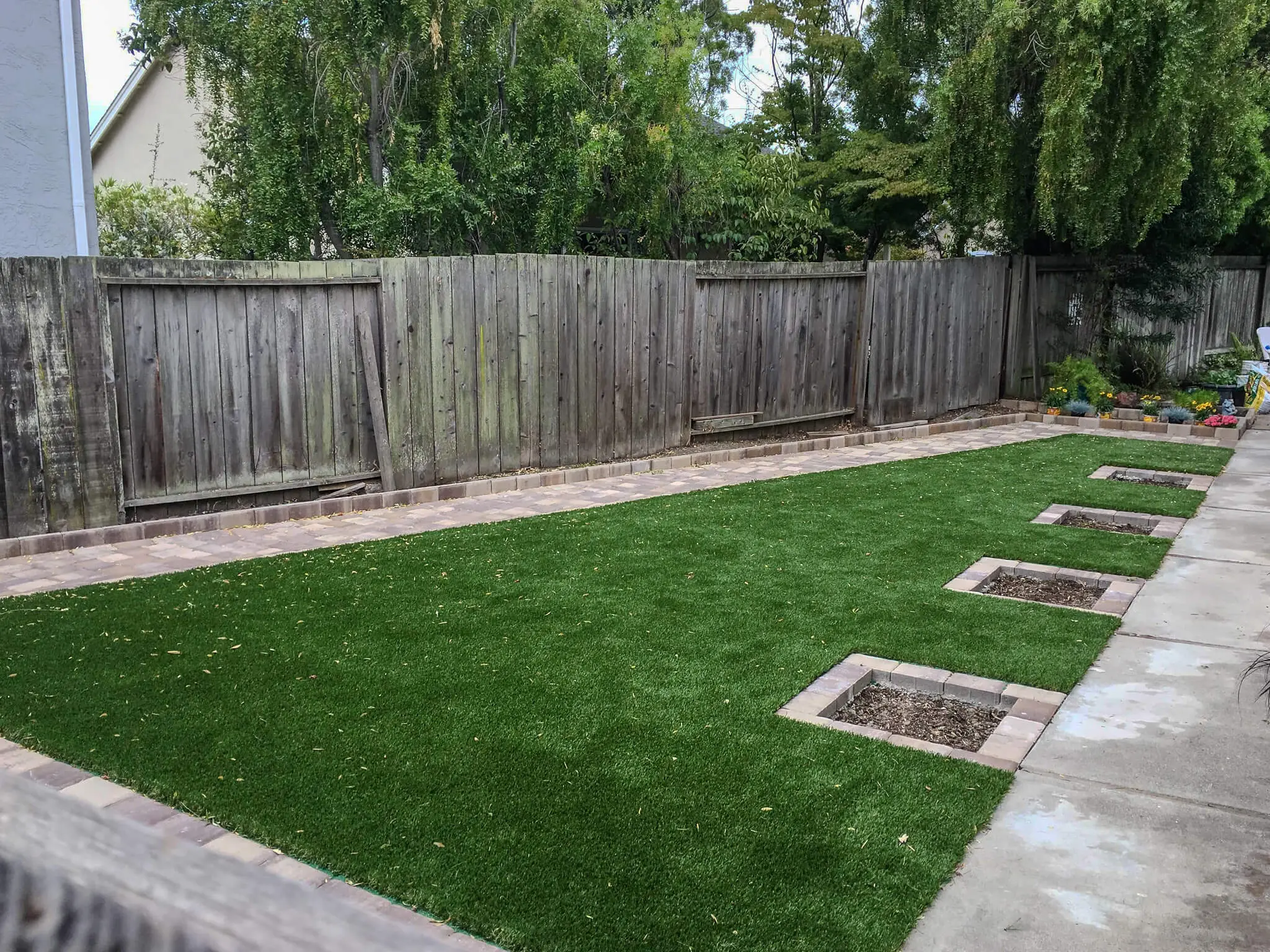 Backyard artificial turf lawn with recessed planter boxes and paver border edging