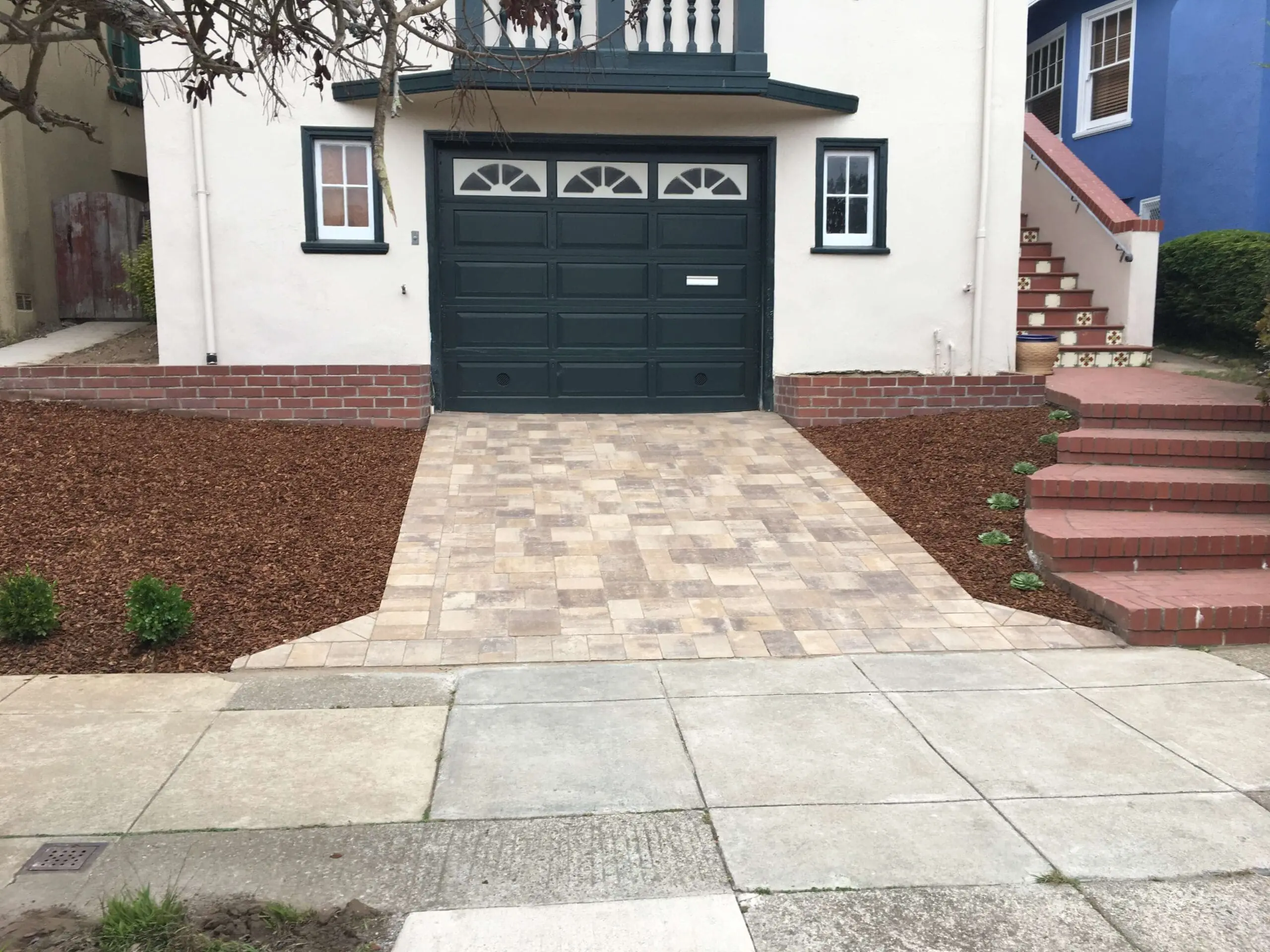 Paver stone driveway apron with wood chip mulch landscaping leading to a garage
