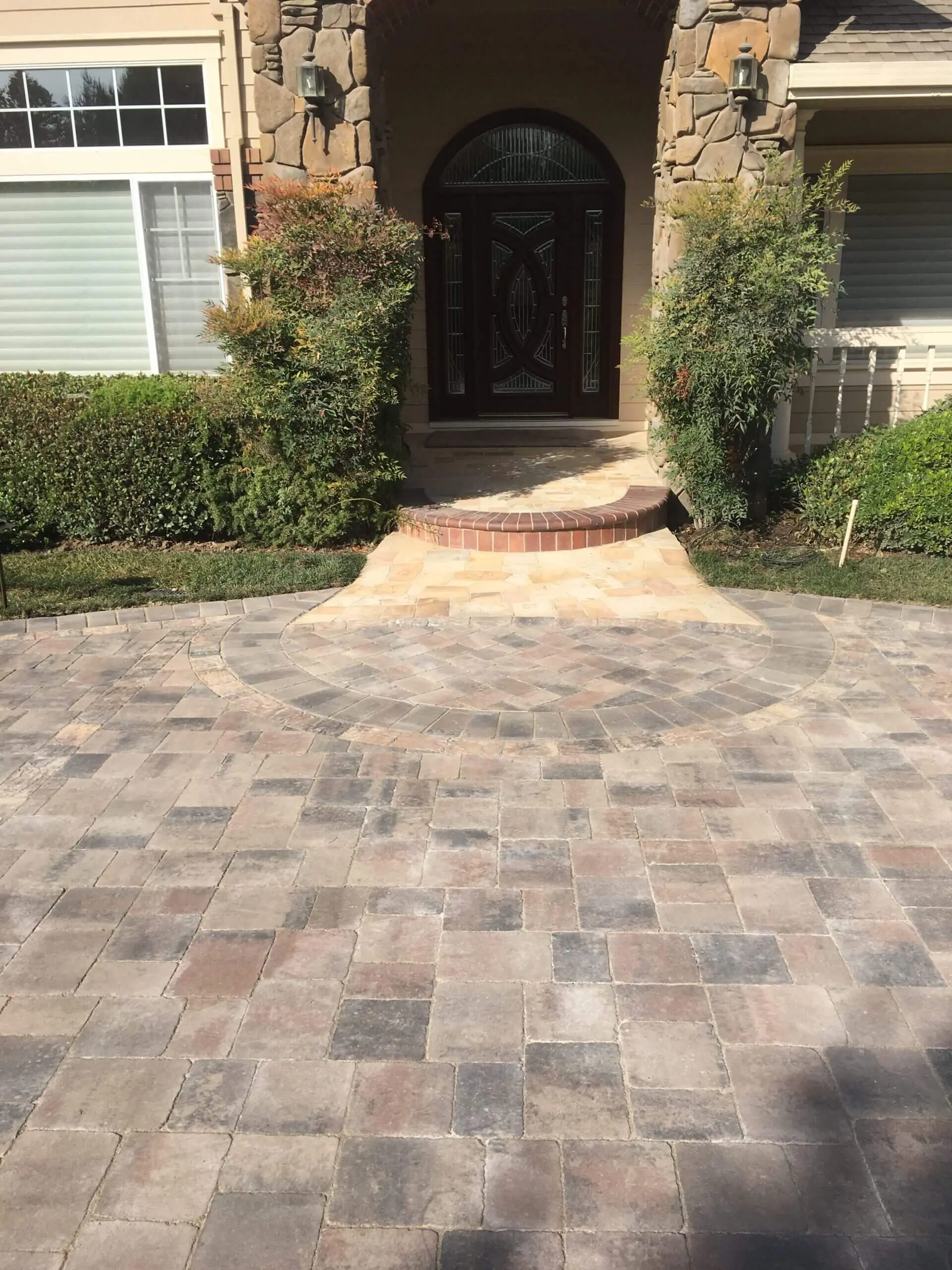 Elegant paver stone driveway leading to a home entrance with arched front door