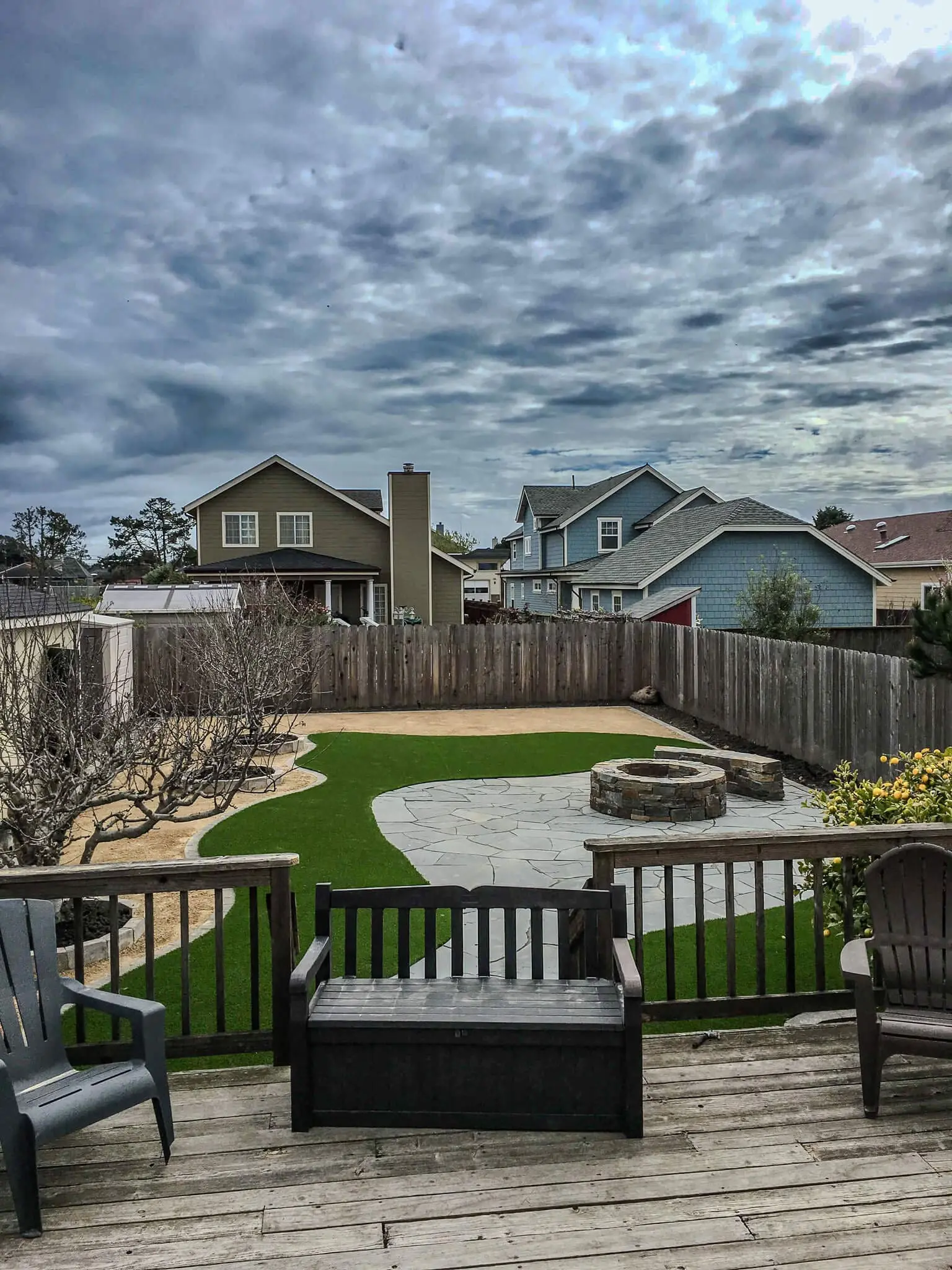 Backyard deck overlooking artificial turf lawn with flagstone patio and stone fire pit