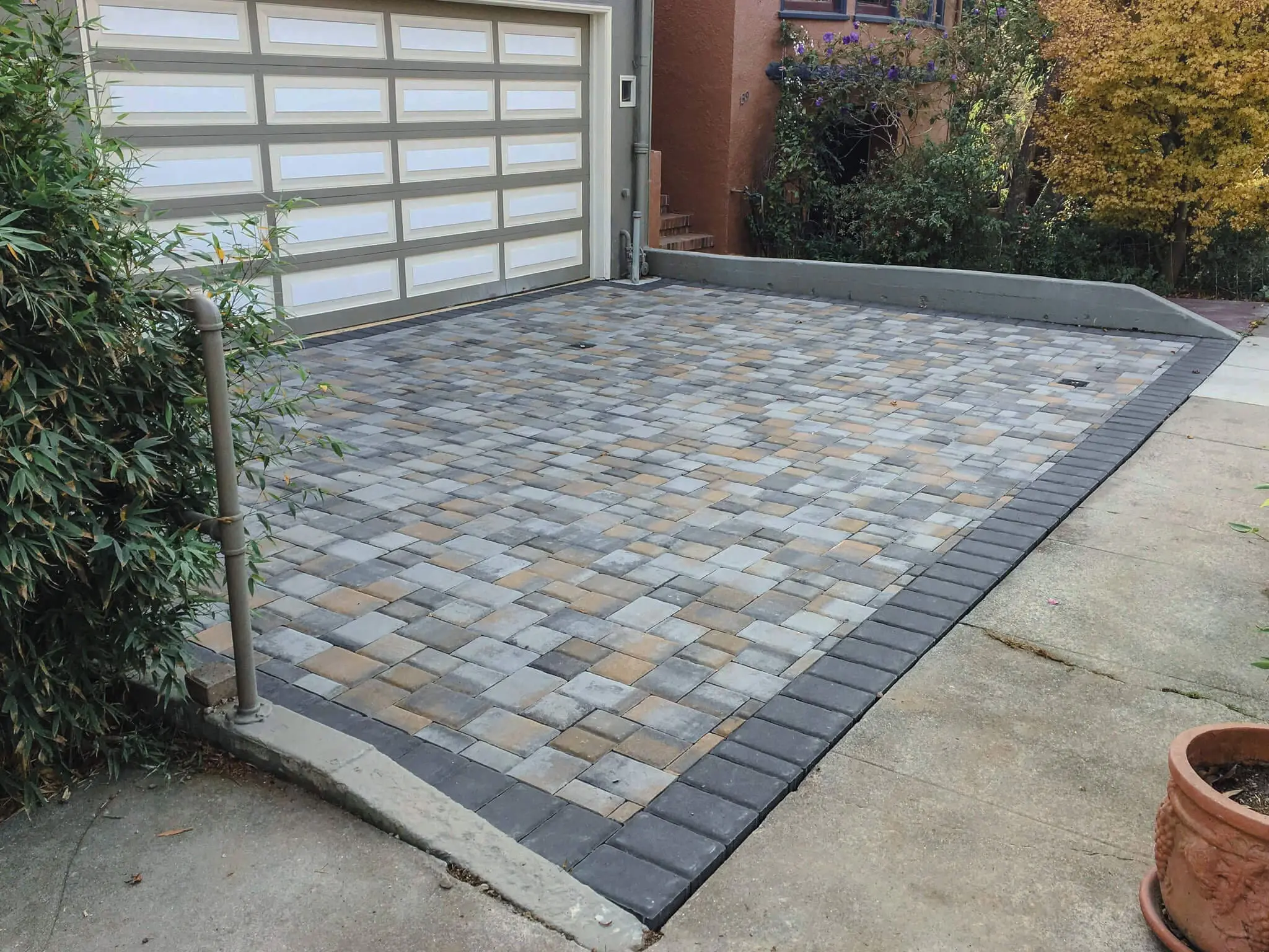 Multi-color cobblestone paver driveway with dark border edging in front of a garage