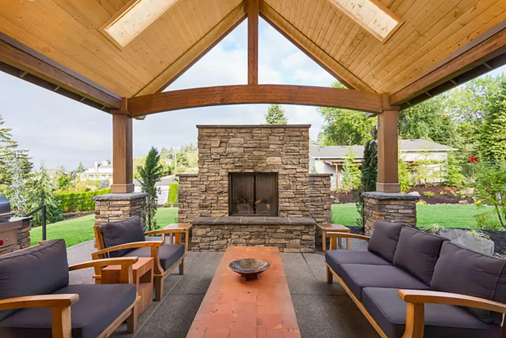 Custom stone outdoor fireplace under a wood-beam pavilion with luxury patio seating in Napa County