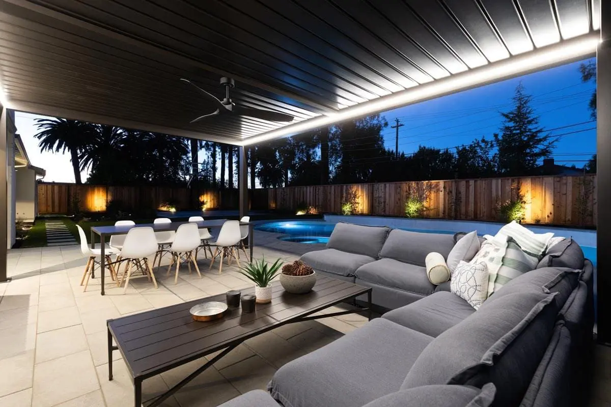 Covered patio with pergola lighting, outdoor sofa, dining table, and pool at dusk