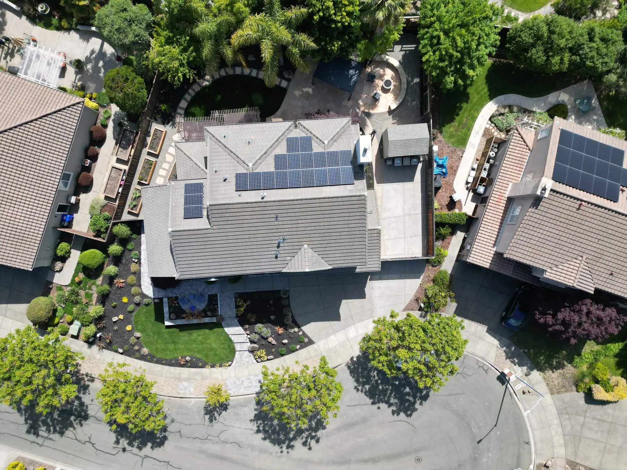 Aerial view of a solar-paneled home by Keystone Yards with a curved front lawn and mulch beds, raised garden boxes along the side yard, and a backyard patio and fire pit, an example of landscape design in Angwin, CA.