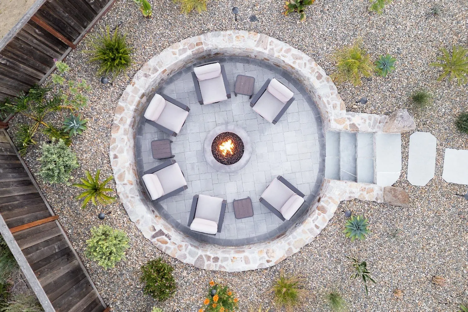 Aerial view of a stone-walled fire pit circle with six lounge chairs, set in a gravel yard with desert plantings, by Keystone Yards.