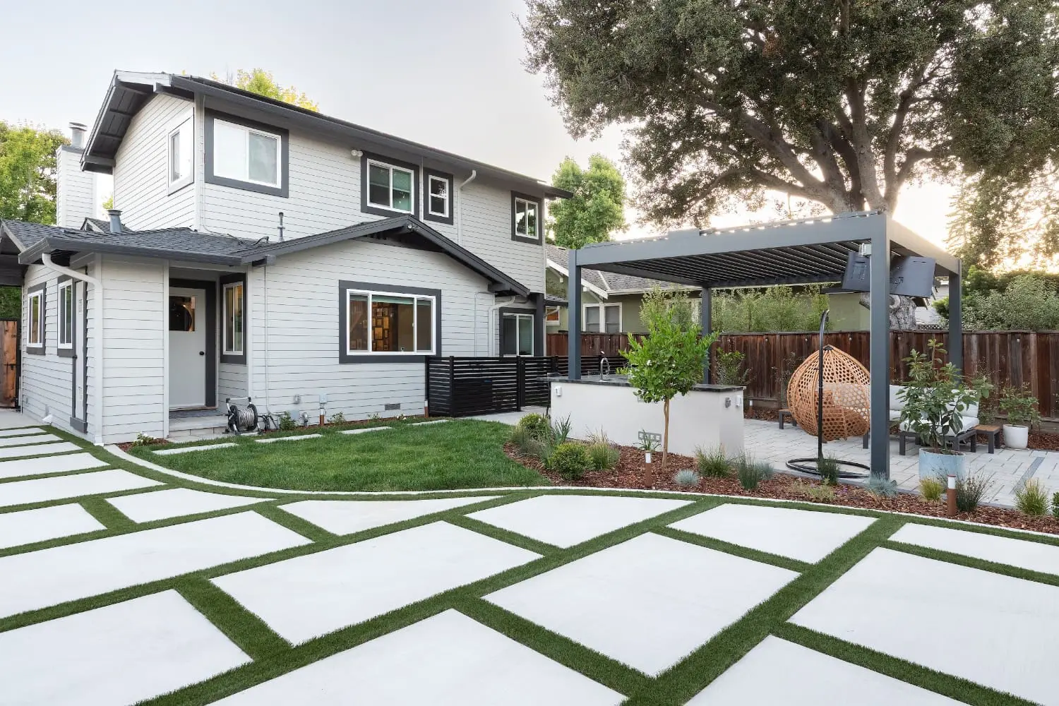 Modern backyard landscape design featuring geometric concrete pavers, a metal pergola, and hanging chair by keystone-yards-Outdoor-design