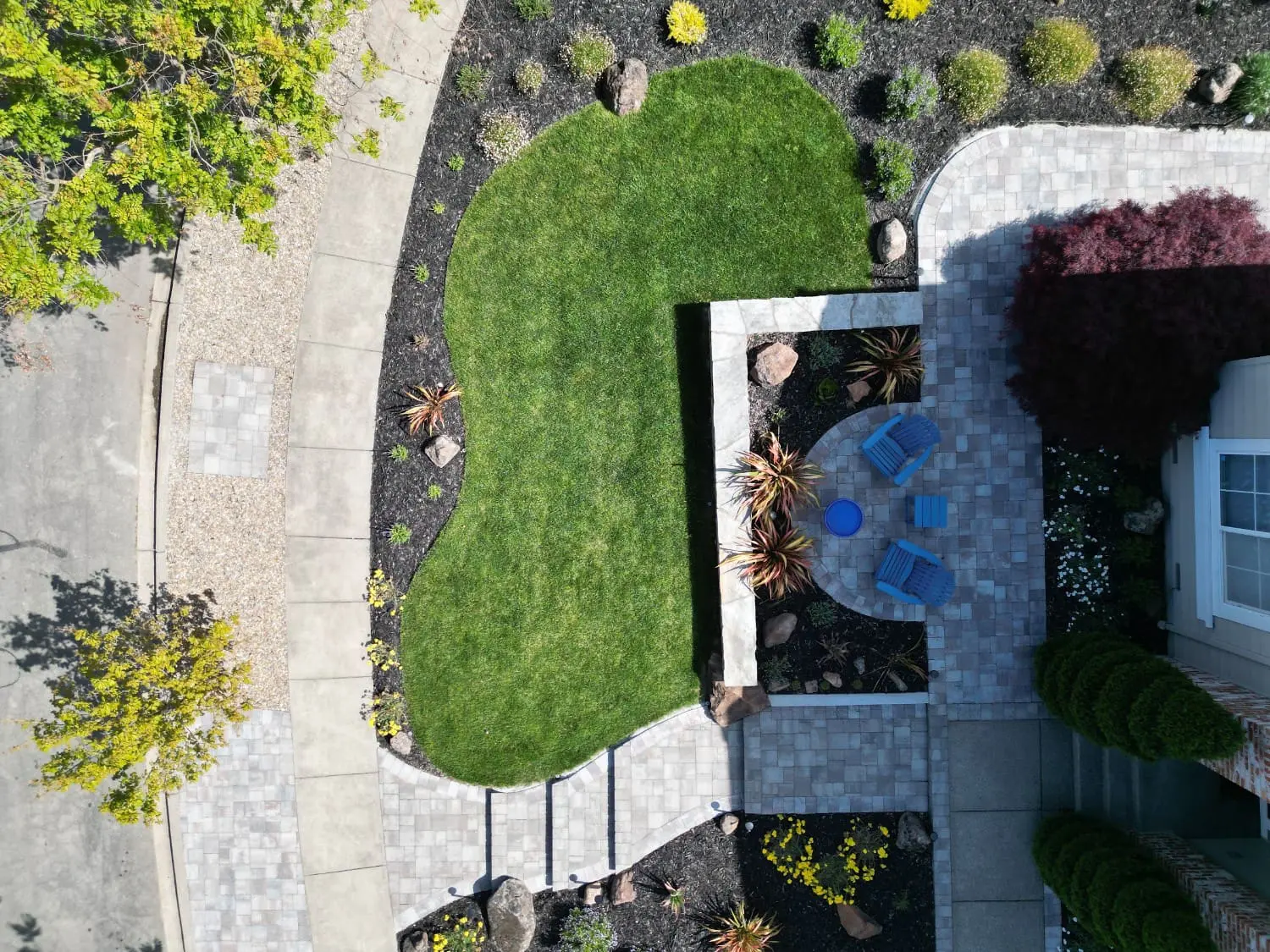 Overhead view of a custom backyard hardscaping design with a stone retaining wall, patio, and curved paver walkway by keystone-yards-Outdoor-design