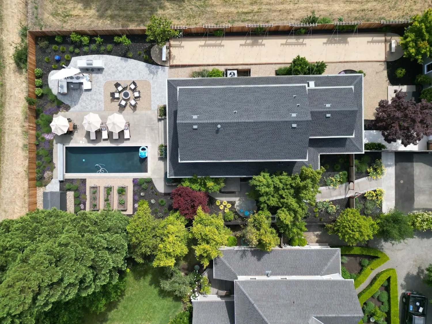 Aerial view of a backyard by Keystone Yards with a lap pool and lounge chairs, a fire pit dining patio, an outdoor kitchen, raised garden beds, and a vineyard trellis beside the house, an example of outdoor design in Napa, CA.