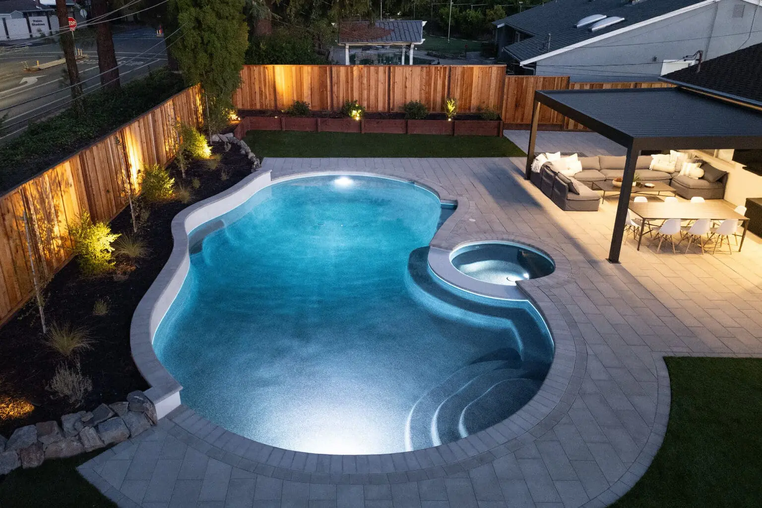 Custom design-build backyard landscape featuring a glowing swimming pool, paver patio, and modern covered pergola in Napa, CA.
