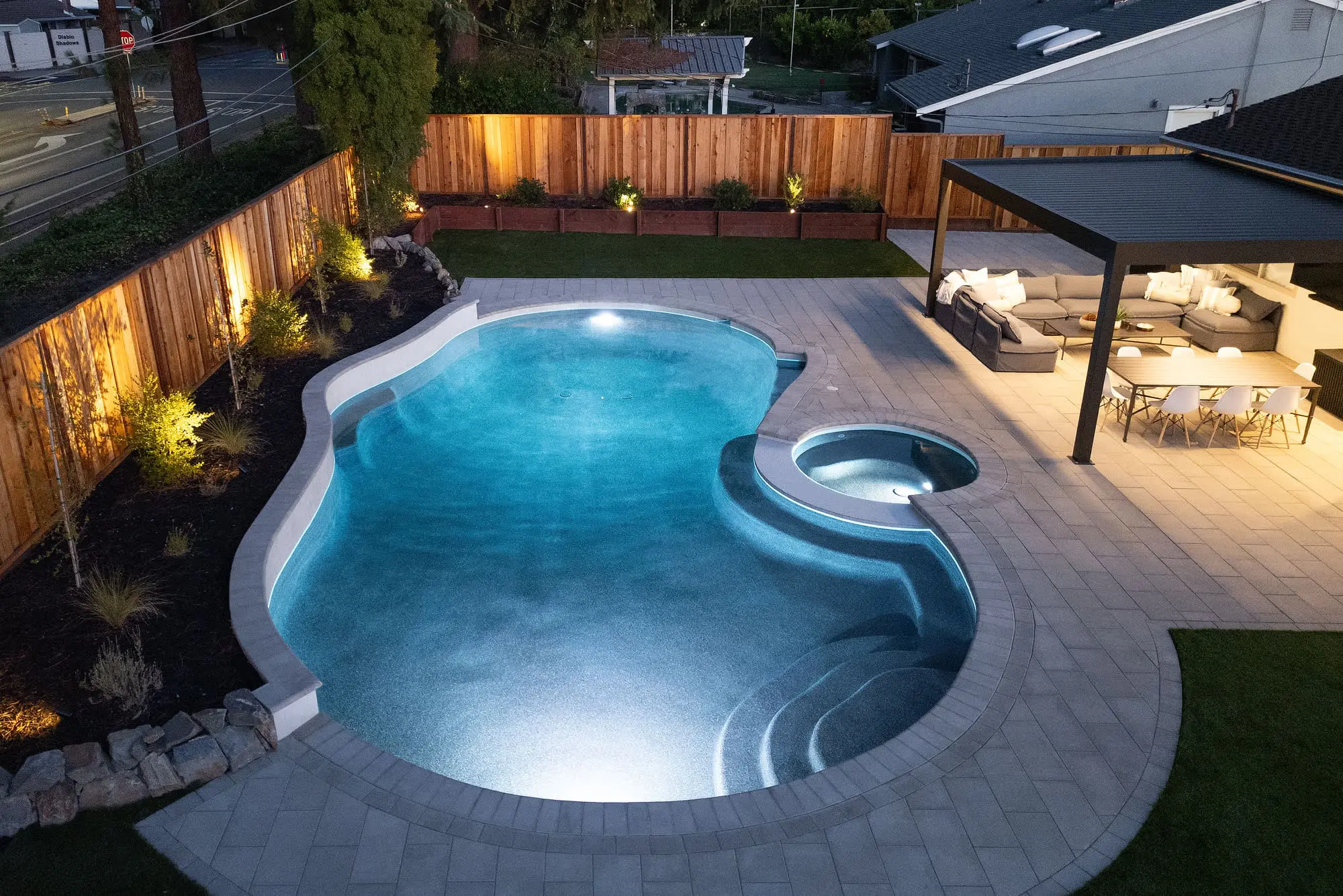 Custom design-build backyard landscape featuring a glowing swimming pool, paver patio, and modern covered pergola in Napa, CA.
