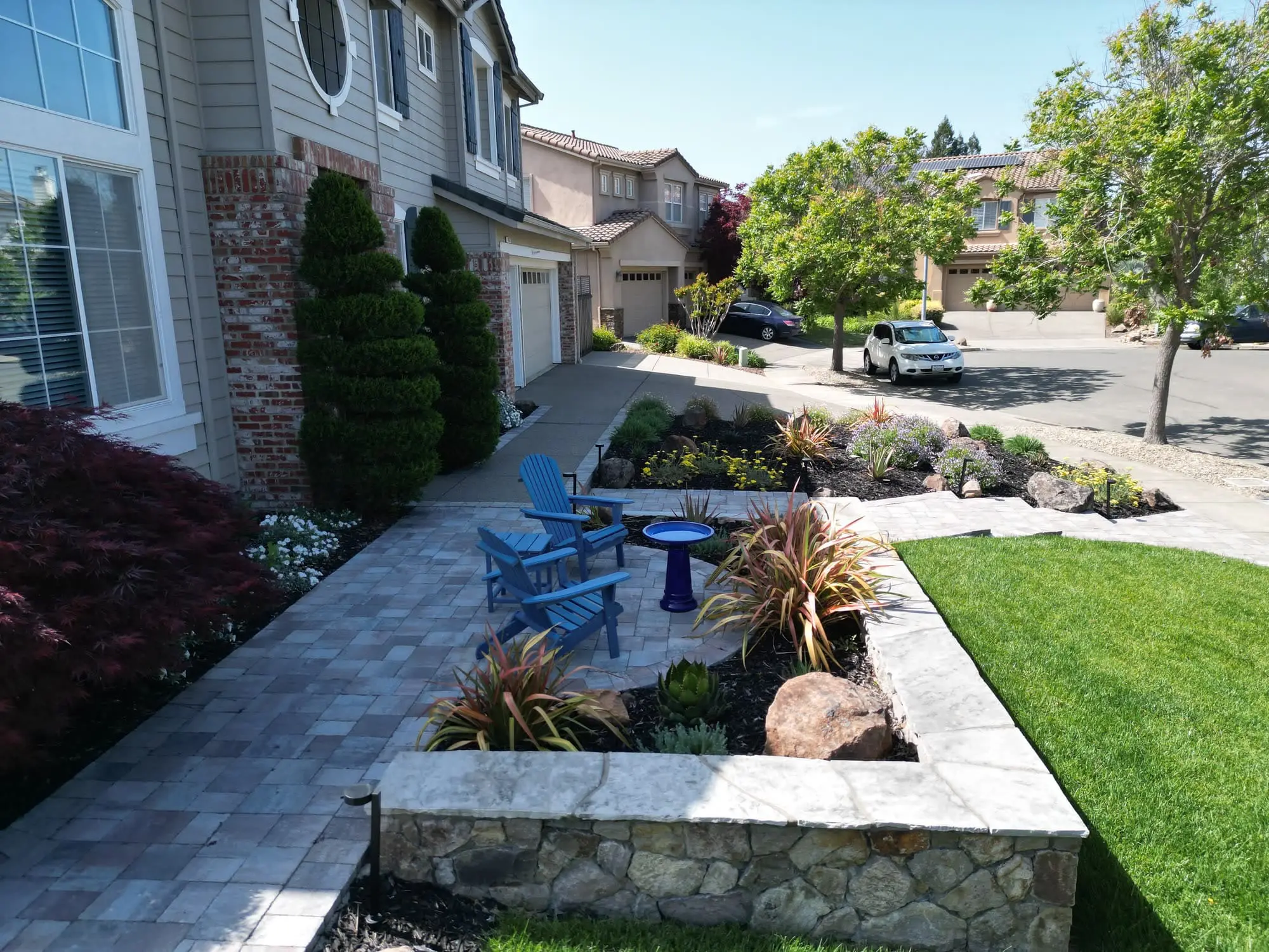Professional front yard landscape design in Napa, CA featuring a stone retaining wall, paver patio, blue Adirondack chairs, and custom garden beds.