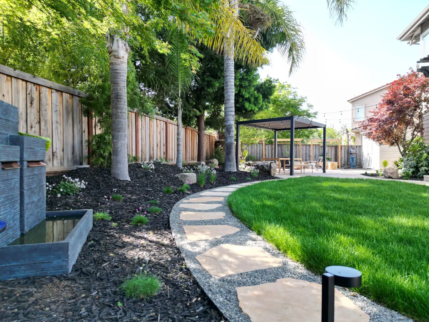 Modern backyard landscape design featuring a stone water feature, curved paver walkway, and lush lawn installed by keystone-yards-saint-helena-ca