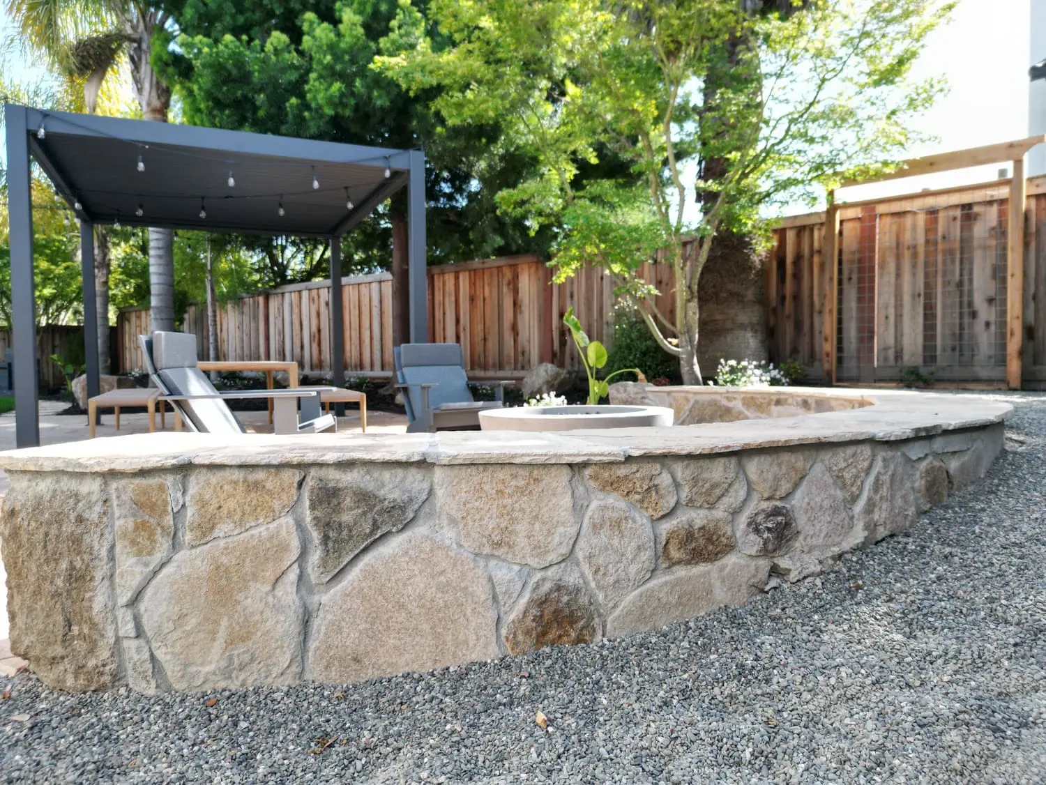 Curved natural stone retaining wall and modern outdoor pergola setup with lounge chairs designed by keystone-yards-sausalito-ca