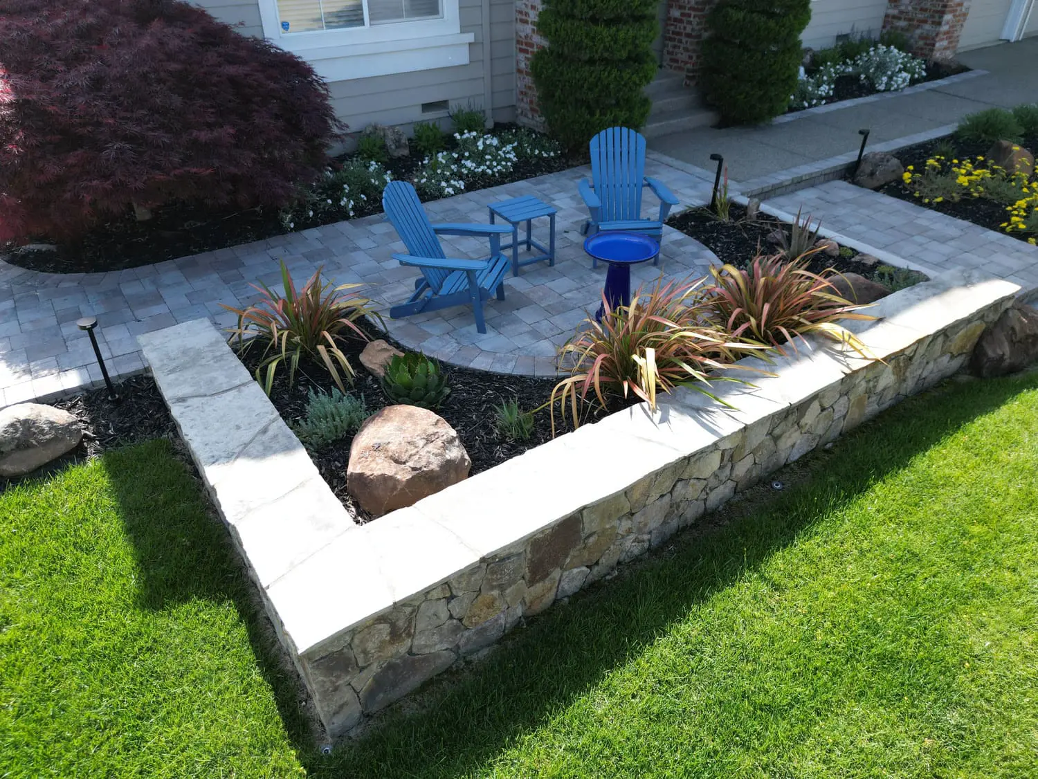 aised natural stone retaining wall and custom patio featuring blue chairs and ornamental grasses designed by keystone-yards-sonoma-ca