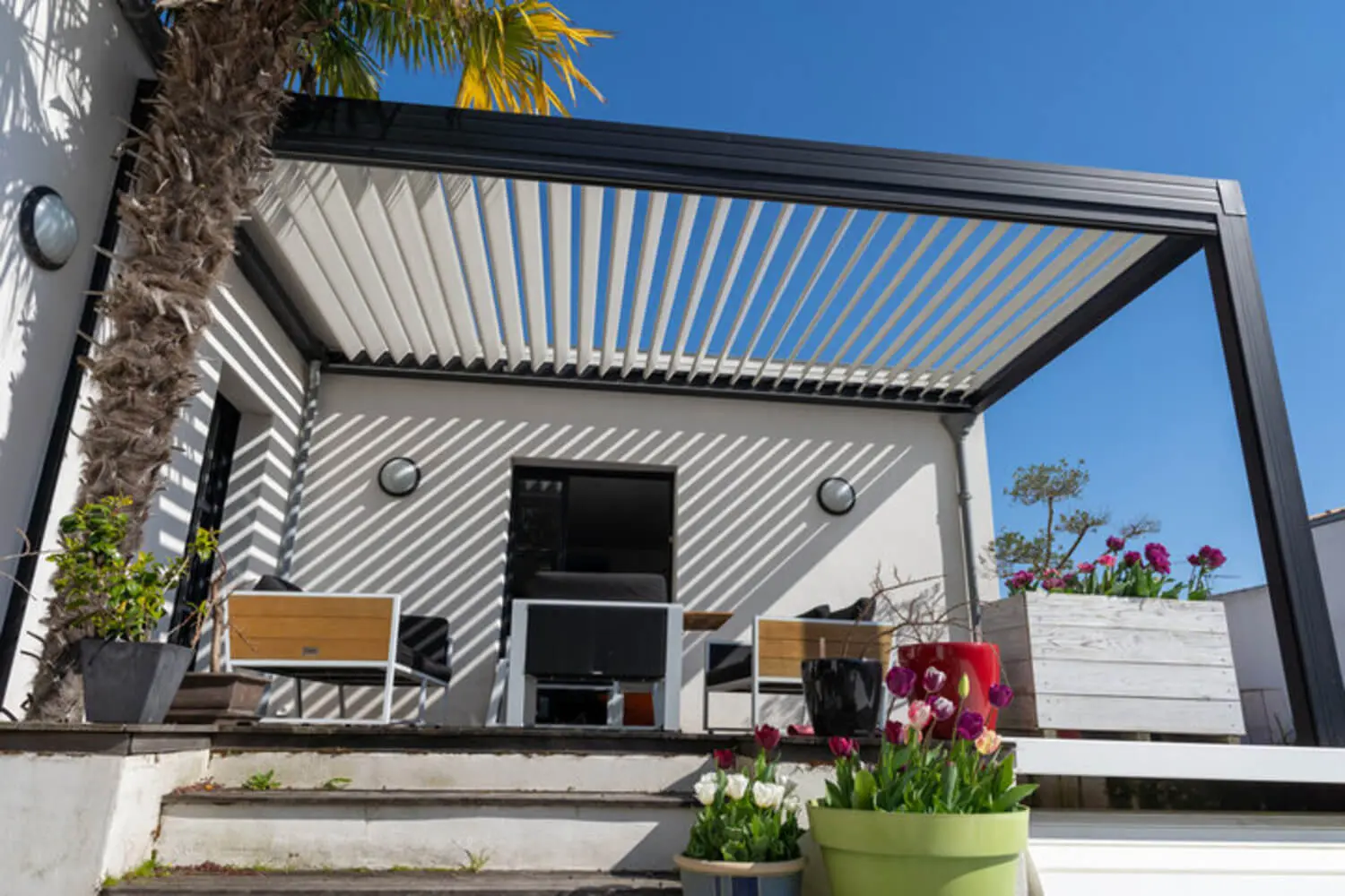 Adjustable louvered pergola roof casting shadow patterns over a sunny outdoor patio.