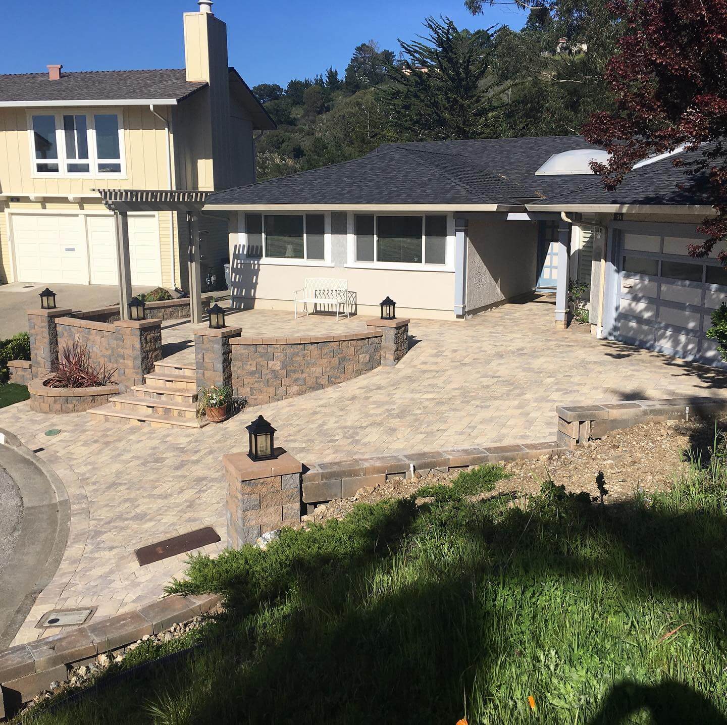 Front yard paver patio with stone retaining walls, lantern posts, and pergola entry
