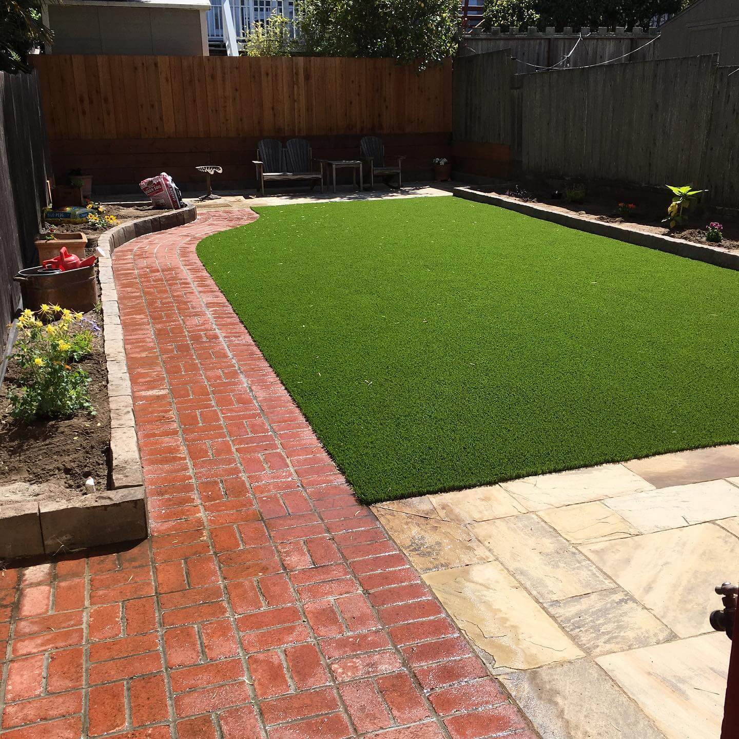 Backyard artificial turf lawn with curved red brick pathway and raised garden beds