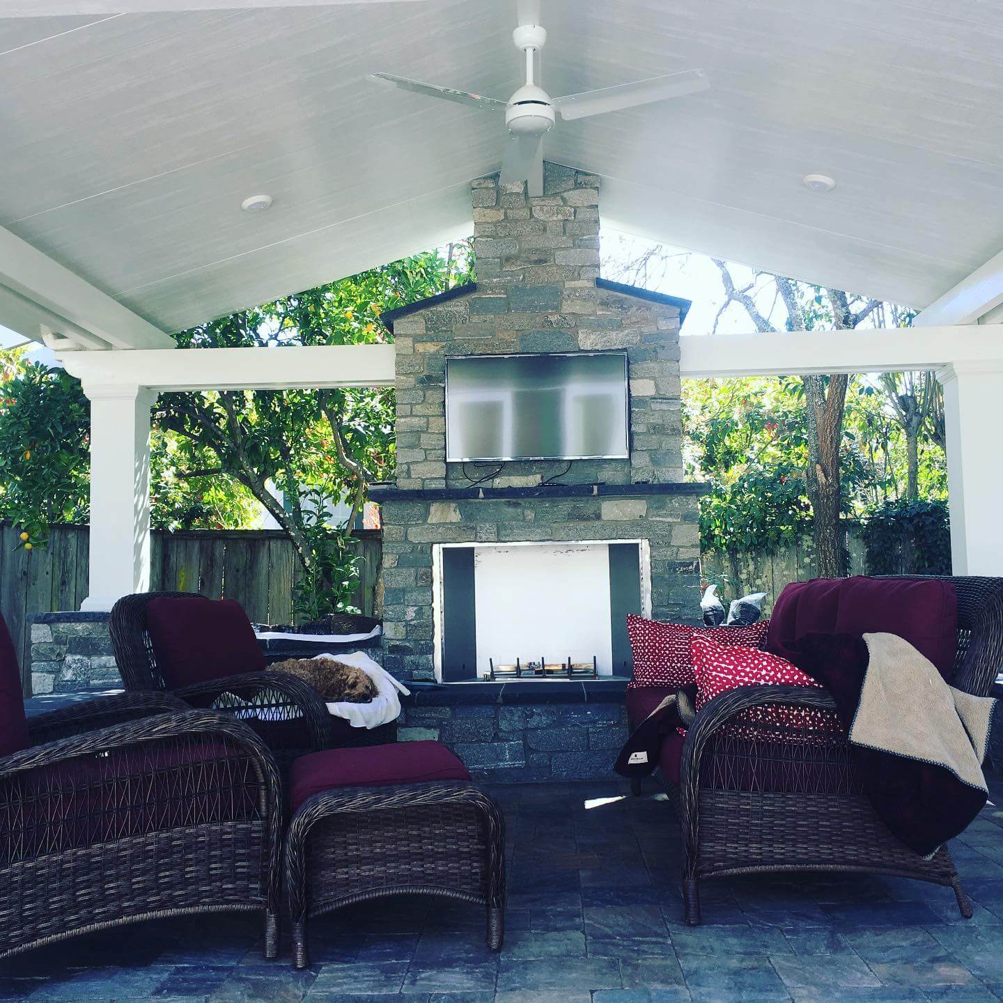 Covered outdoor patio with stone fireplace, mounted TV, and wicker lounge chairs