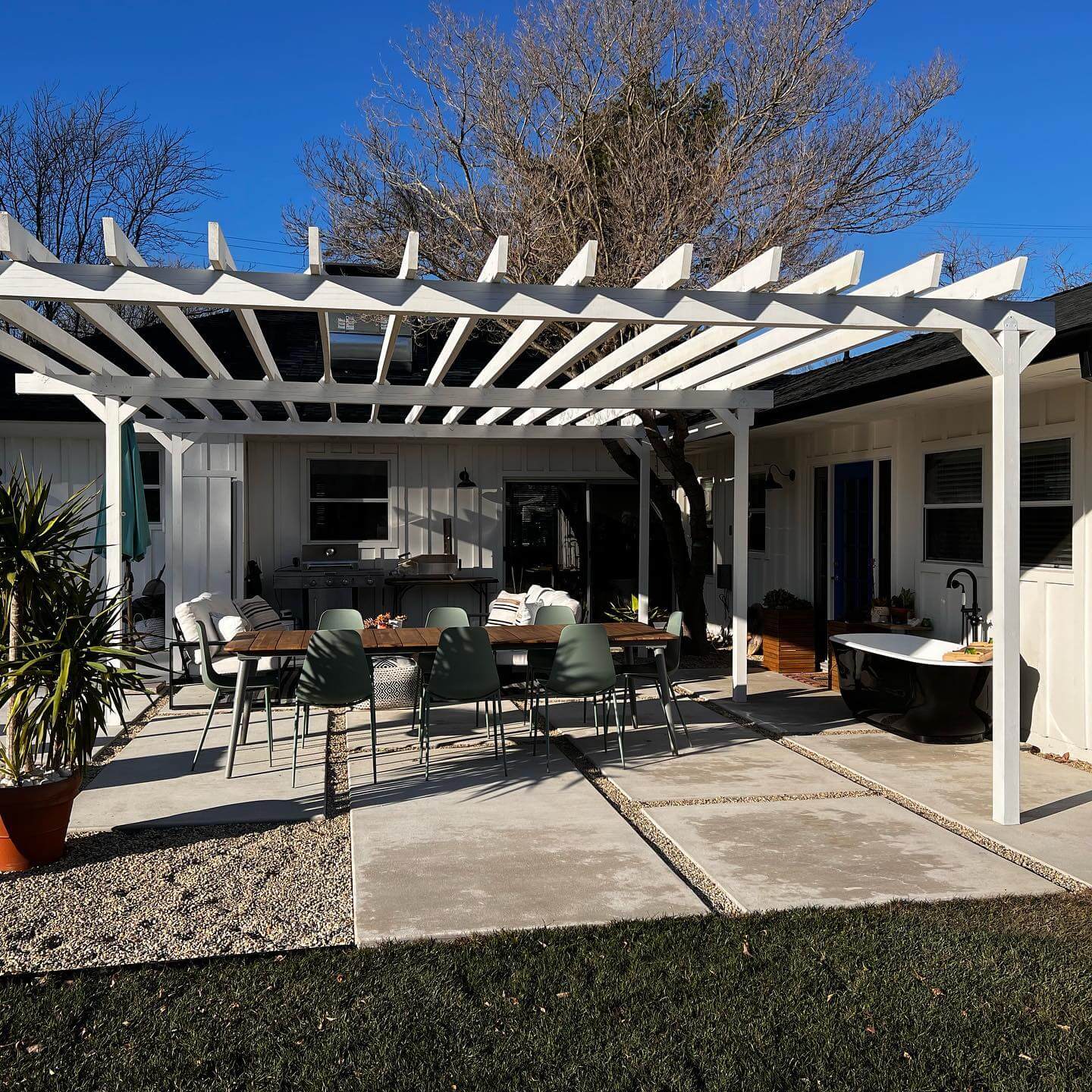 White pergola covering an outdoor dining area with patio furniture and concrete pavers
