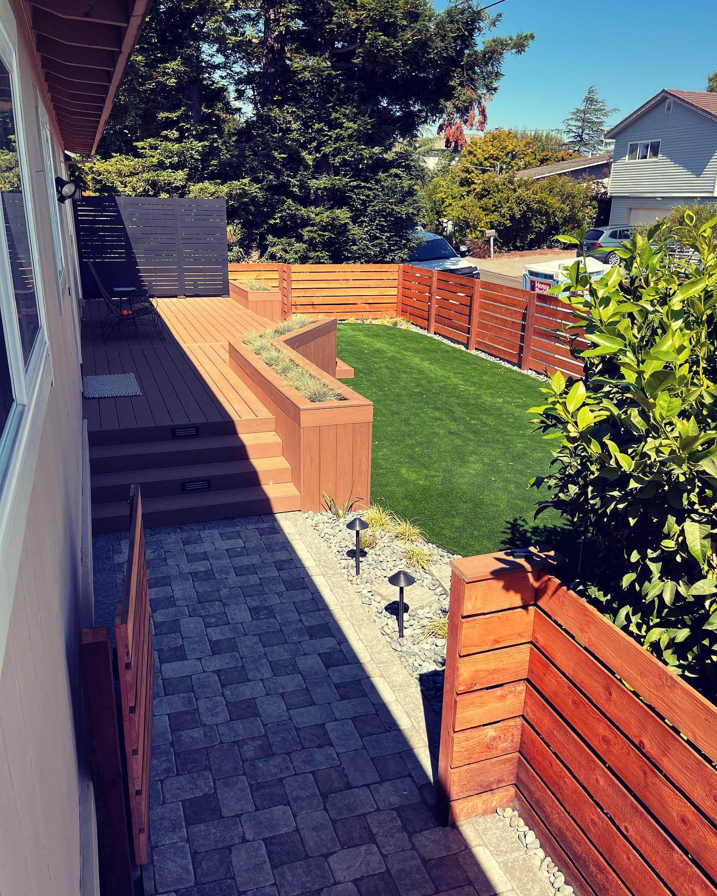 Modern backyard with wood deck, raised planters, artificial turf, and paver pathway