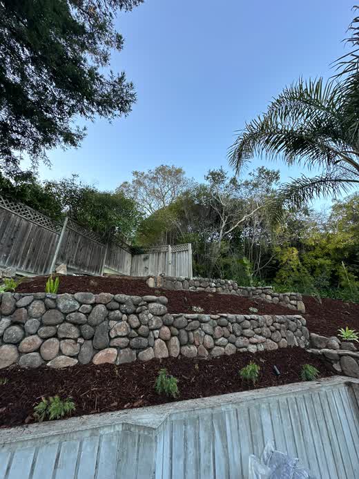 Custom backyard landscape renovation featuring terraced natural stone retaining walls and fresh mulch beds in Napa, CA.