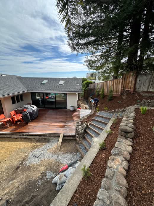 Custom backyard renovation featuring a wooden deck patio, natural stone retaining walls, and outdoor stairs in Napa, CA.