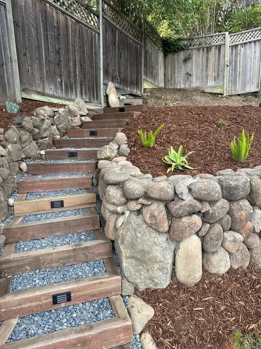 Custom backyard renovation featuring natural stone retaining walls and wooden steps with integrated lighting in Napa, CA.