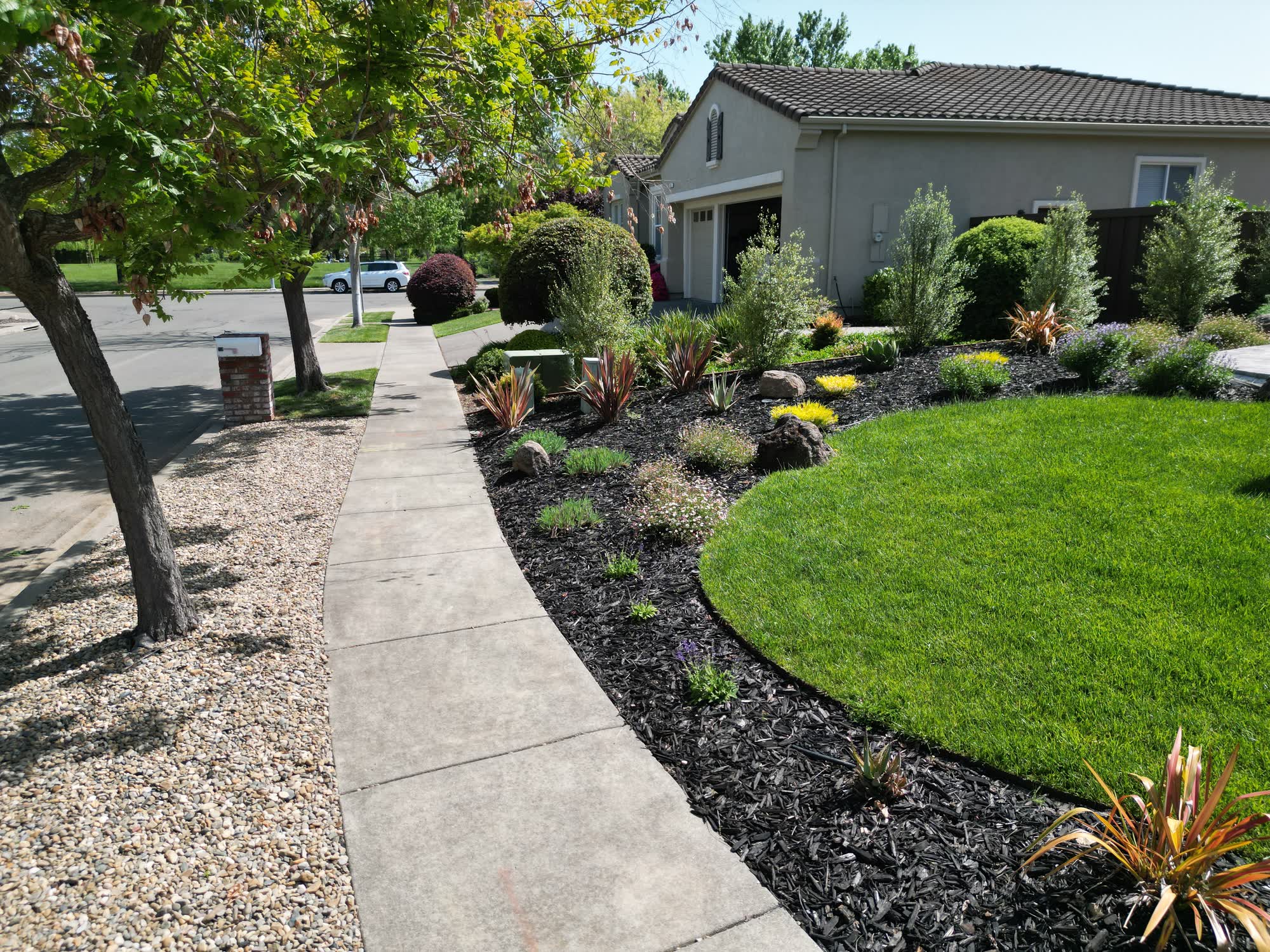 Professional front yard landscape design featuring a neatly manicured green lawn, dark mulch flower beds, and decorative shrubs by Keystone Yards.