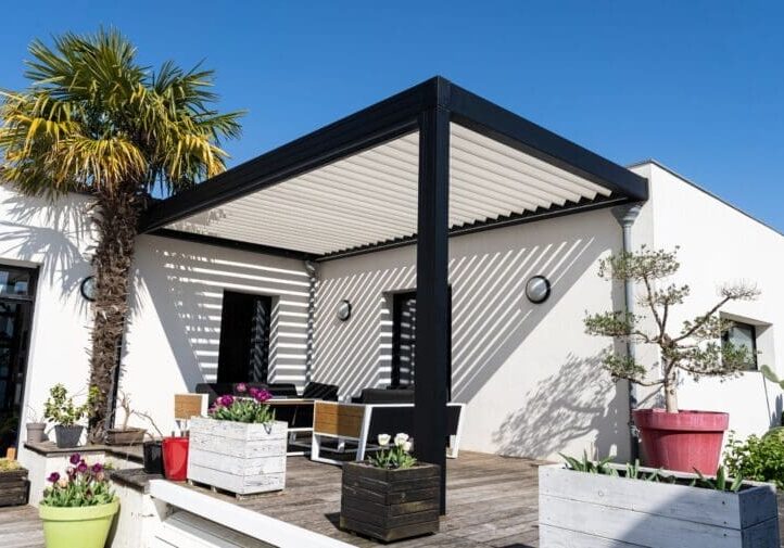 Modern black louvered pergola with wood deck, potted flowers, palm tree, and contemporary outdoor seating area