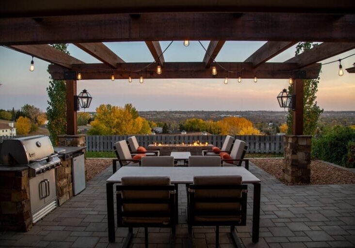 Pergola with string lights, outdoor dining, fire pit seating, and grill at sunset
