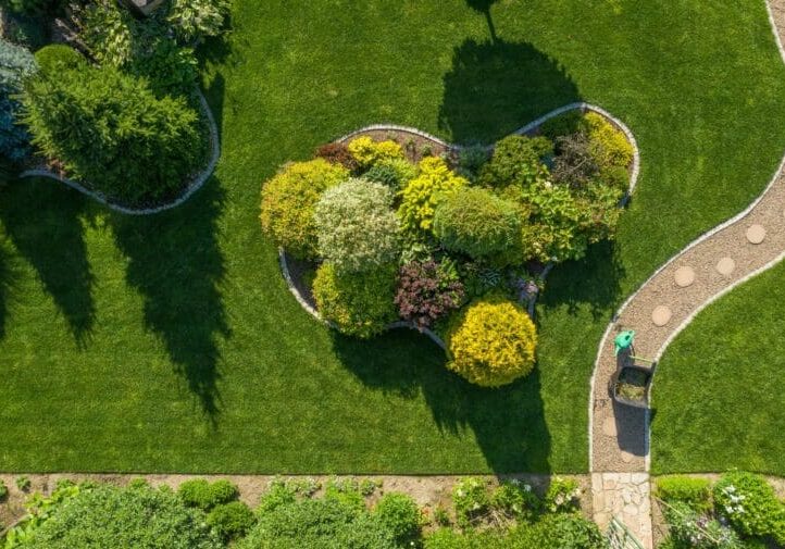 Aerial view of a professionally designed backyard with curved garden island, ornamental shrubs, and winding stone pathway