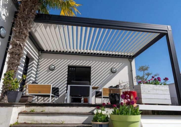 Adjustable louvered pergola roof casting shadow patterns over a sunny outdoor patio.