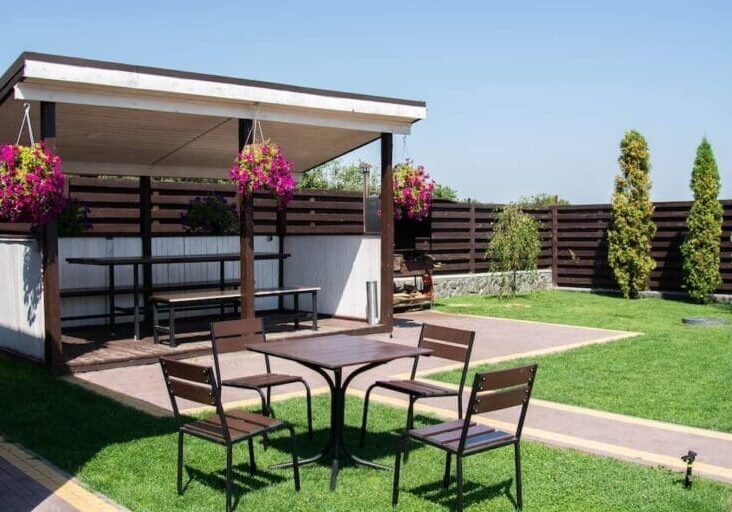 Backyard gazebo with hanging flower baskets, outdoor dining table, and manicured lawn