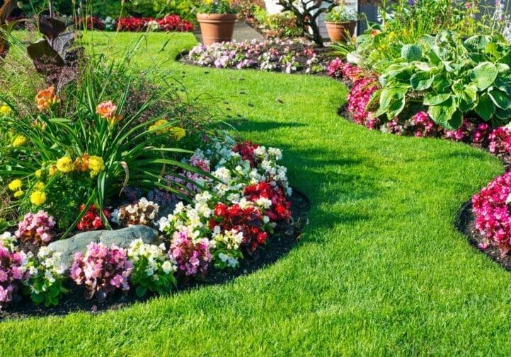 Lush garden with curved flower bed borders, colorful seasonal blooms, and a manicured green lawn pathway