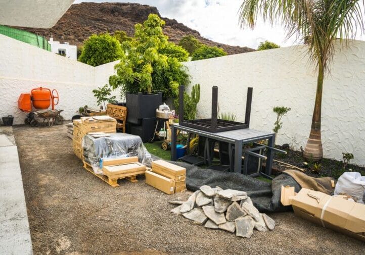 Outdoor remodeling project in progress with stone pavers, building materials, cement mixer, and pergola frame installation