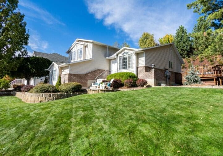 Brick home with terraced stone retaining wall, trimmed shrubs, and lush sloped front yard lawn design