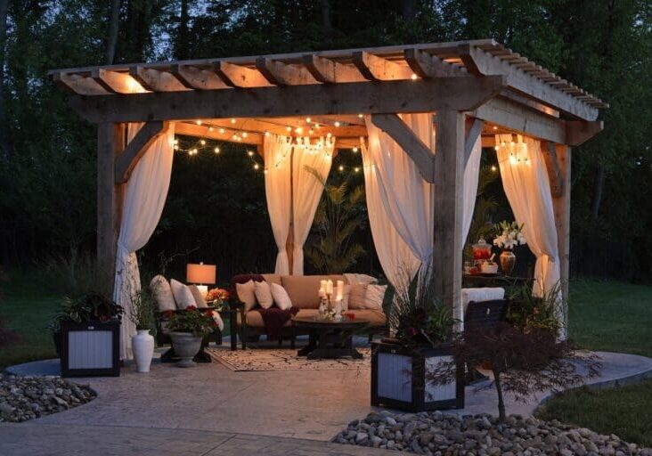 Wood pergola with string lights, flowing curtains, and outdoor lounge seating at night