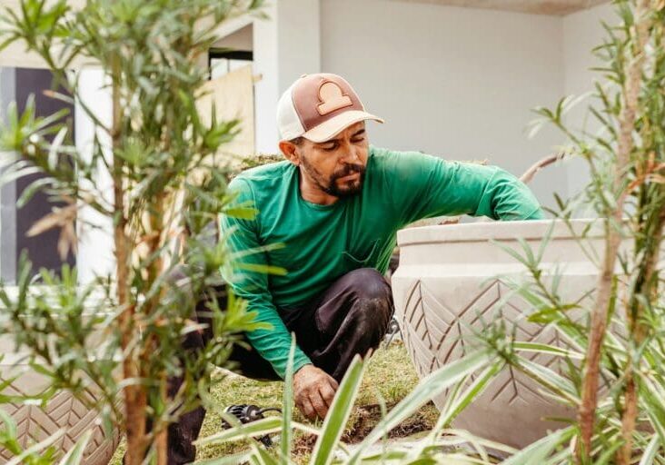 Professional landscaper planting and arranging plants in a decorative outdoor planter surrounded by garden greenery