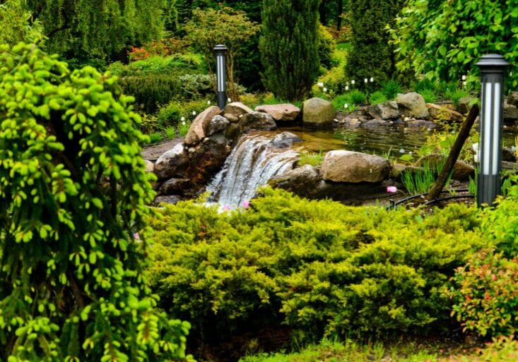 Custom garden water feature with natural stone waterfall, pond, pathway lighting, and lush surrounding greenery