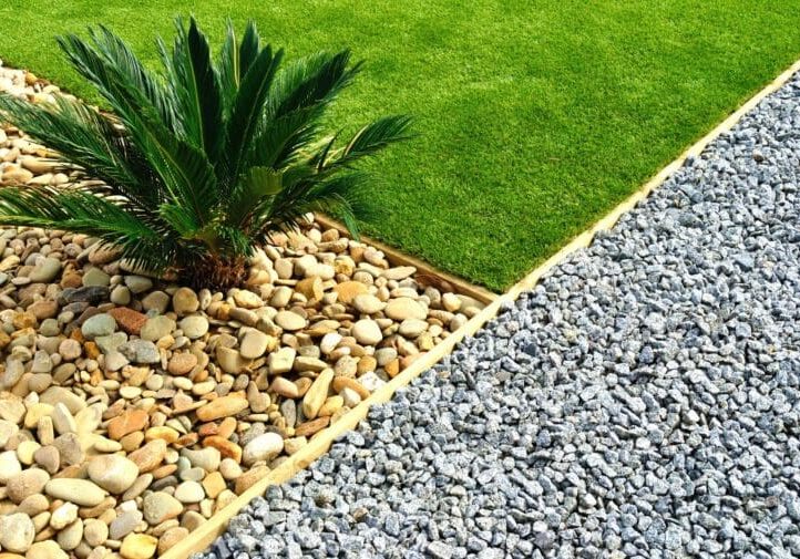 Close-up of a manicured lawn edge with sago palm, river rocks, and crushed gravel ground cover
