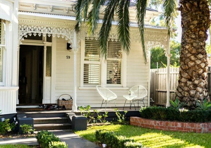 Victorian home front porch with white chairs, palm tree, and brick garden bed