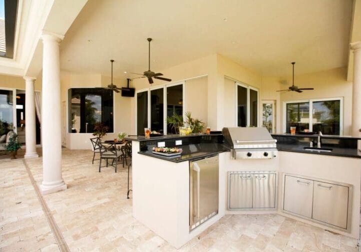 Custom outdoor kitchen with built-in grill, granite countertops, stone tile flooring, and covered patio dining area