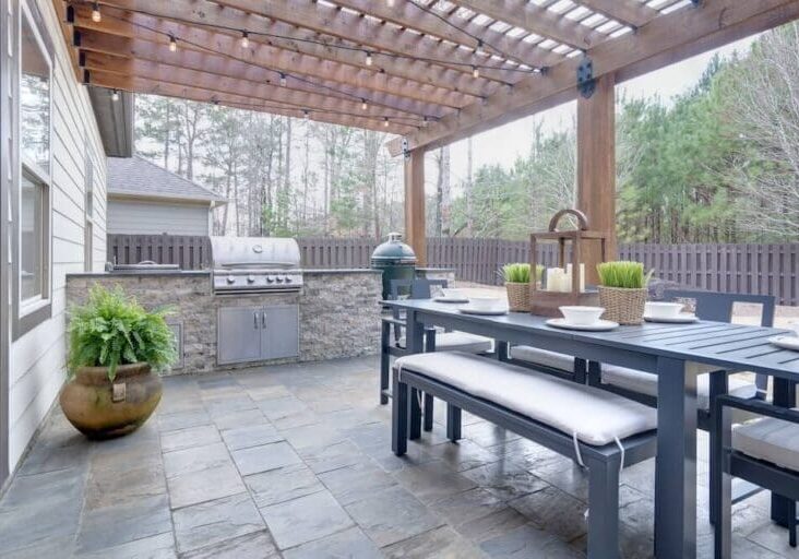 Wood pergola with string lights over an outdoor dining set and stone kitchen with grill