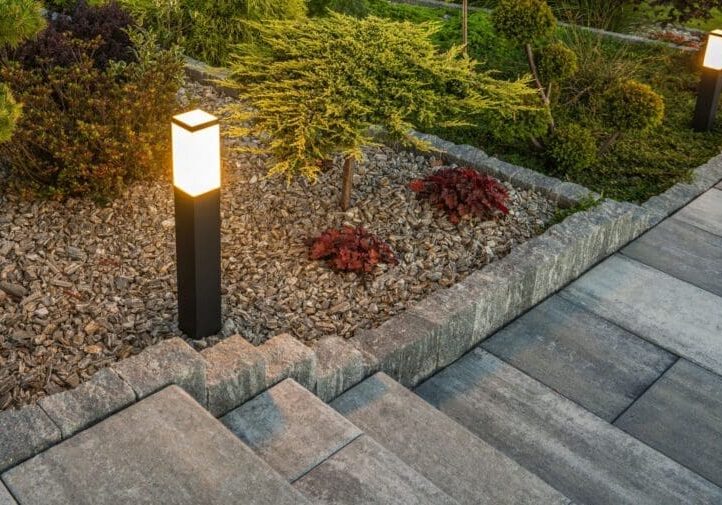 Stone paver steps with modern bollard pathway lighting, decorative gravel bed, and colorful shrub plantings at dusk