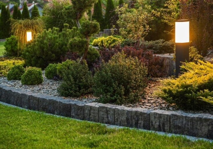 Landscaped garden bed with boulder edging, mixed shrubs, and bollard lighting