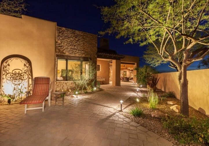 Southwest-style courtyard at night with stone paver pathway, bollard landscape lighting, and ornamental iron gate
